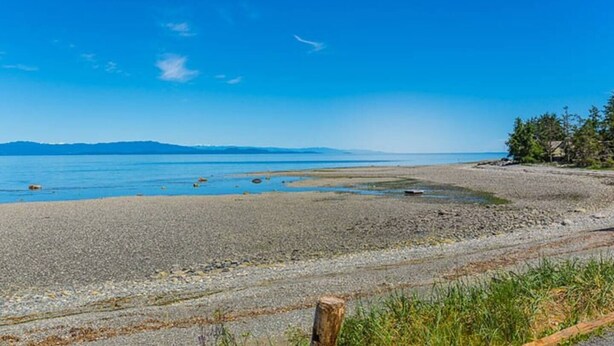 A pebbly beach with calm waters and distant mountains.