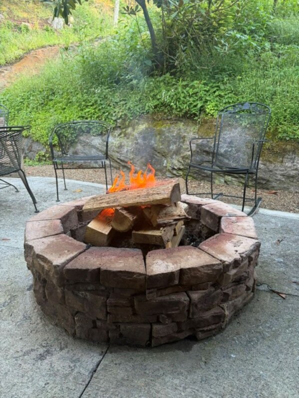 A circular stone fire pit with logs, surrounded by metal chairs.