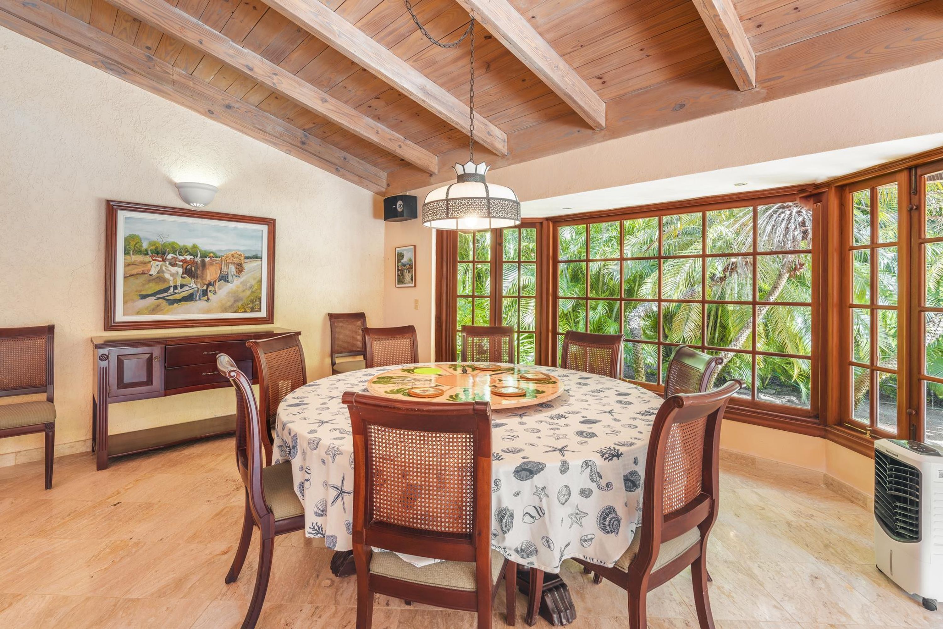 A dining area with a round table, chairs, and a large window with a view of greenery.