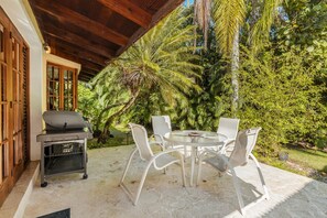 Een terras buiten met een ronde tafel en stoelen, een barbecue en weelderige beplanting.