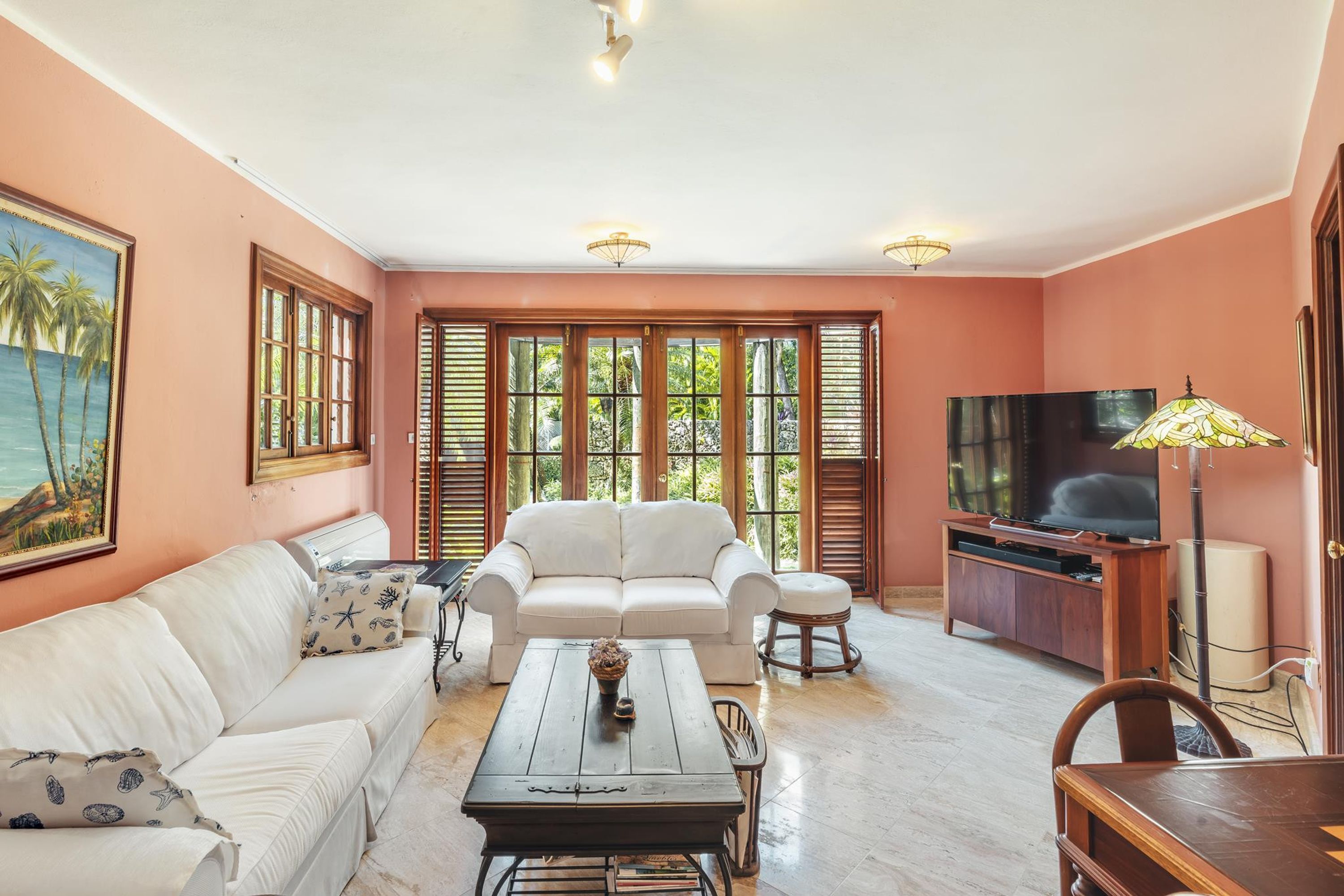 Ein Wohnzimmer mit einem weißen Sofa, einem Couchtisch, einem Fernsehschrank und großen Fenstern mit Rollläden.