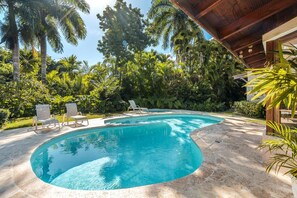 Ein Schwimmbecken mit zwei Liegestühlen und einer Holz-Pergola.
