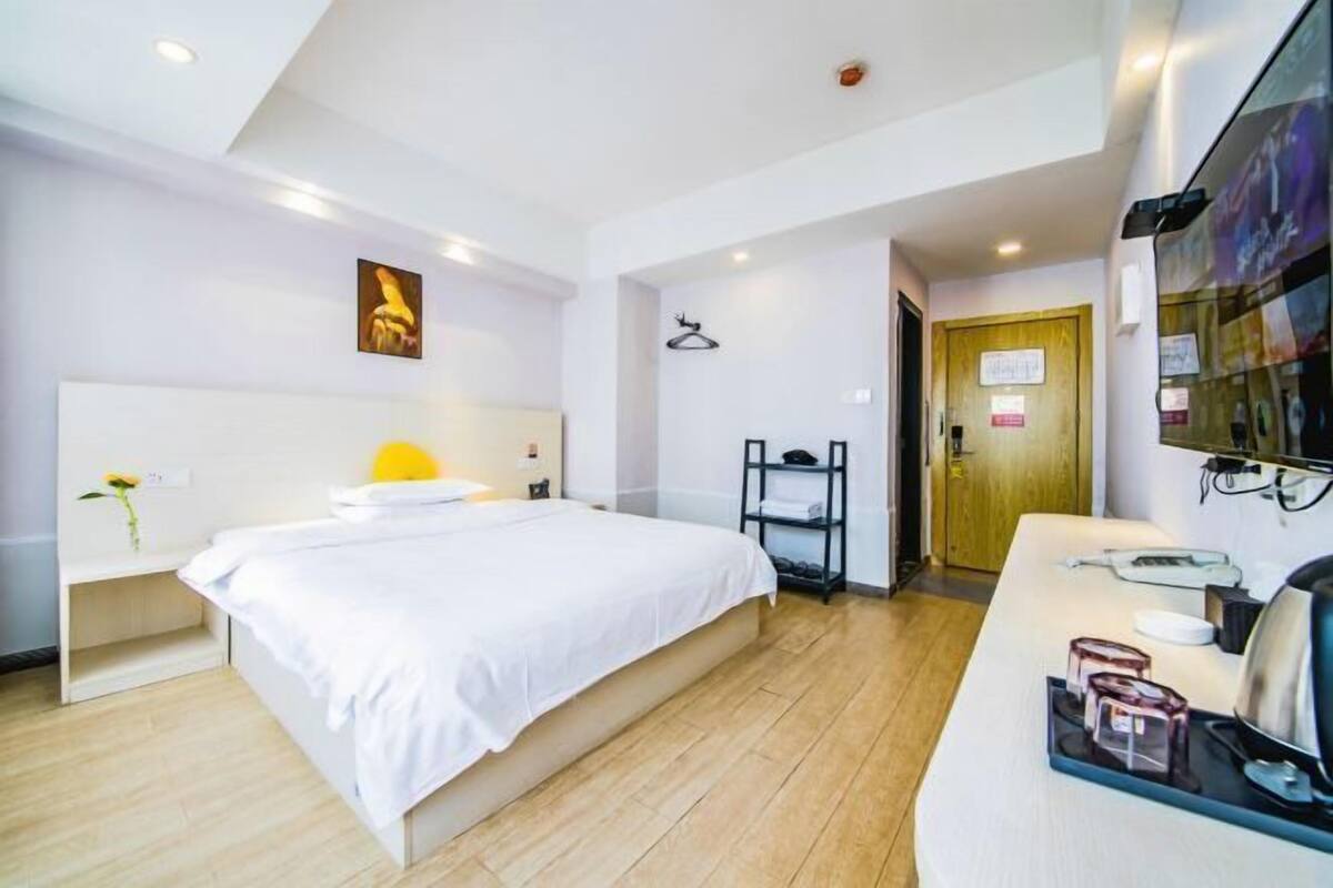 A hotel room with a bed, bedside table, a desk with a chair, a mirror, and a door.