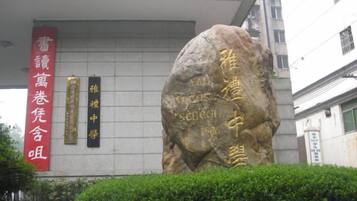 Un monumento de piedra con inscripciones, un estandarte rojo con caracteres chinos y un edificio al fondo.