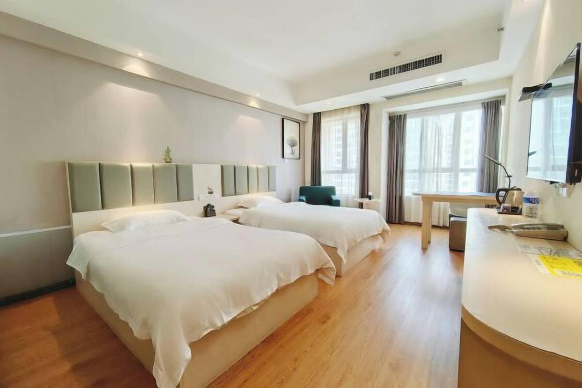 A hotel room with two beds, a desk, a chair, and a TV.