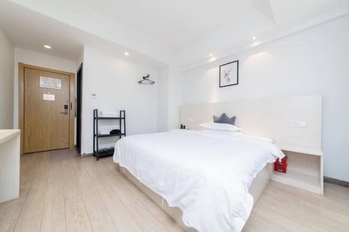 A bedroom with a large bed, a wooden door, a shelf with shoes, and a framed picture on the wall.