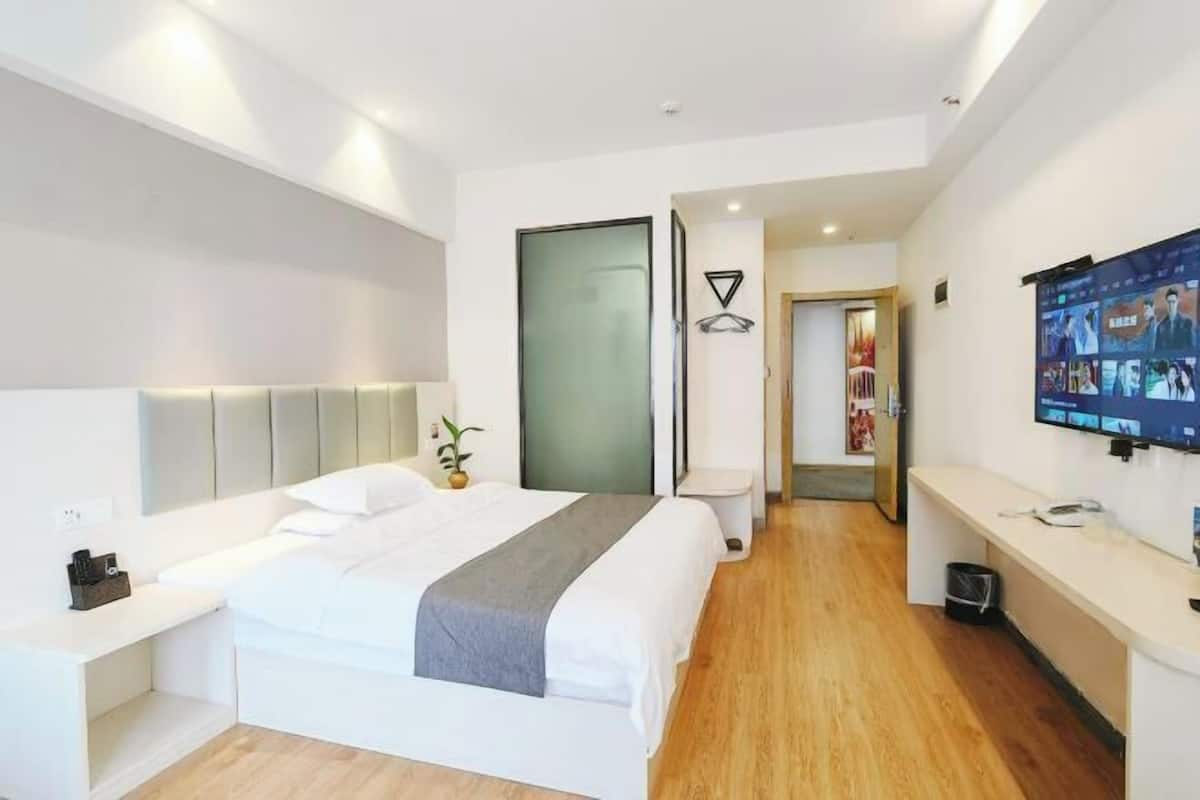 A modern hotel room with a large bed, bedside tables, a TV, and a door leading to a hallway.