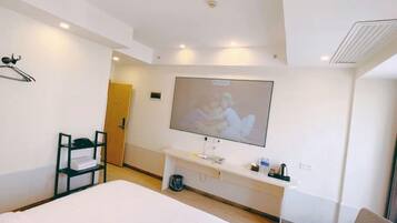 Habitación de hotel con una cama, un televisor montado en la pared, un escritorio con silla y una mesita de noche con lámpara.
