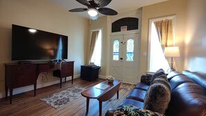 Ein Wohnzimmer mit Flachbildfernseher, Holzmöbeln, Deckenventilator und einer Tür mit Buntglasfenster.