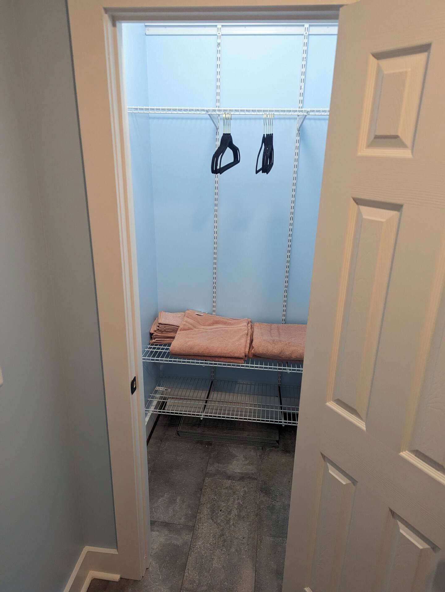 A walk-in closet with shelves and hanging space, featuring a folded towel and a pair of shoes.