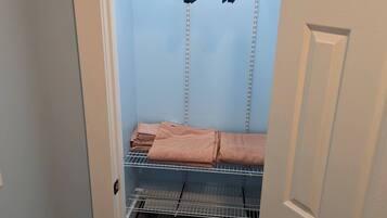 A walk-in closet with shelves and hanging space, featuring a folded towel and a pair of shoes.