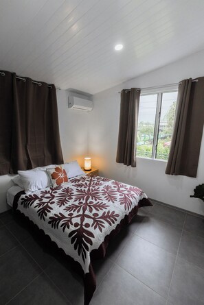 Ein Schlafzimmer mit Bett, Vorhängen, einem Nachttisch mit Lampe und einem Fenster mit Vorhängen.