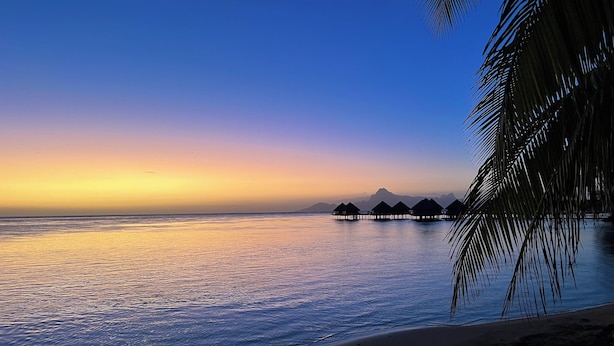 A beach with overwater bungalows and a clear sky.
