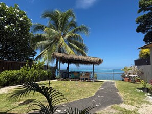 A pathway leading to a beachside area with palm trees, a thatched structure, and a view of the ocean. - Beachfront Home Puna'auia Tahiti (Punaauia)