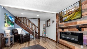 A living room with a fireplace, a sofa, a coffee table, a bookshelf, and a painting on the wall. - Lux 3BR home - Views/Wildlife/RMNP/Shop/Snowshoe (Estes Park)