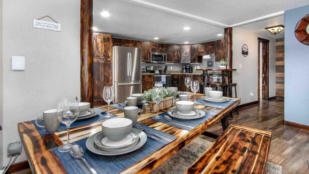 A modern kitchen with dark wood cabinets, stainless steel appliances, and a long dining table set for six. - Lux 3BR home - Views/Wildlife/RMNP/Shop/Snowshoe (Estes Park)