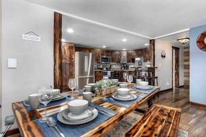 Una cocina moderna con alacenas de madera oscura, electrodomésticos de acero inoxidable y una larga mesa de comedor preparada para seis personas.