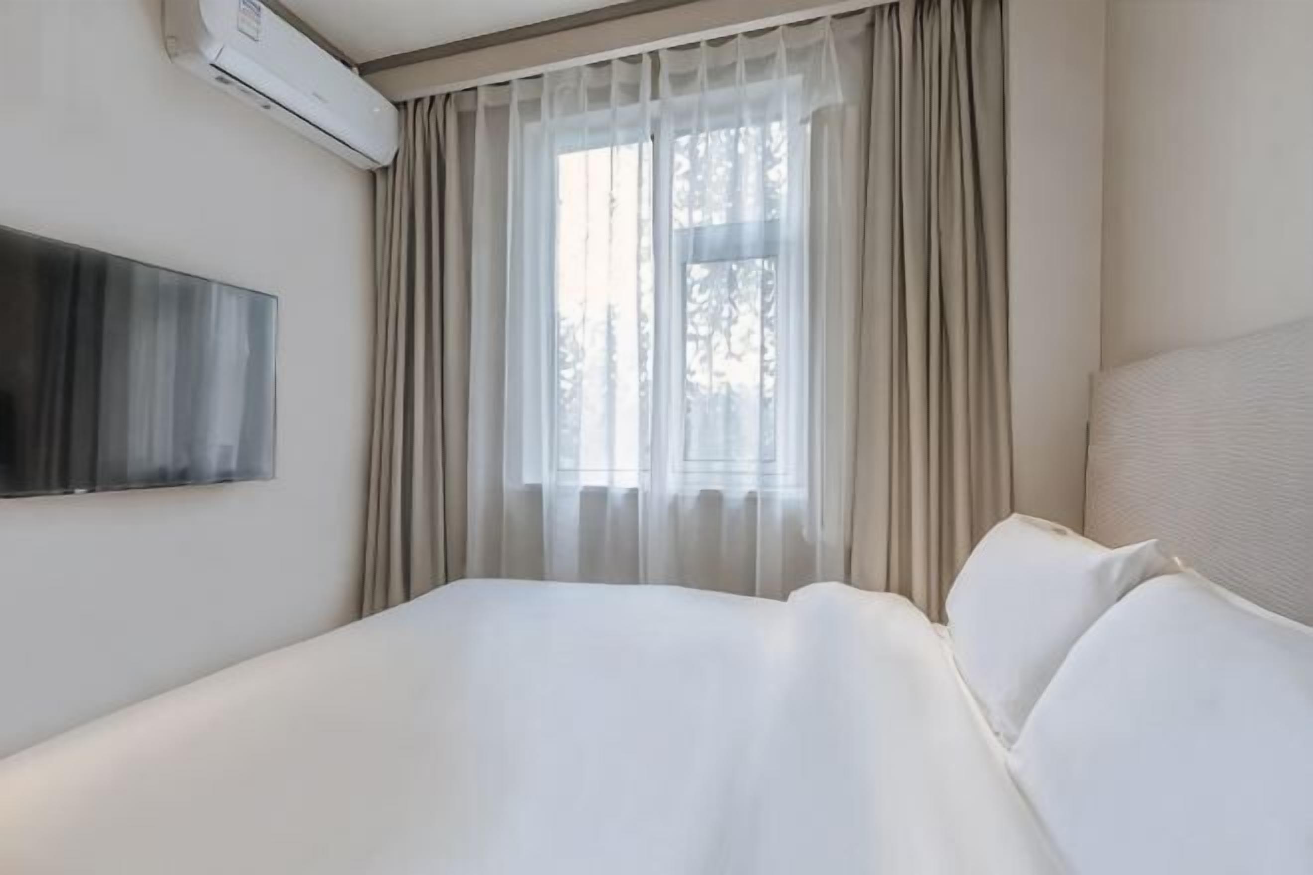 A hotel room with a bed, a TV mounted on the wall, and a window with curtains.