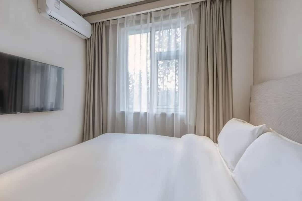 A hotel room with a bed, a TV mounted on the wall, and a window with curtains.