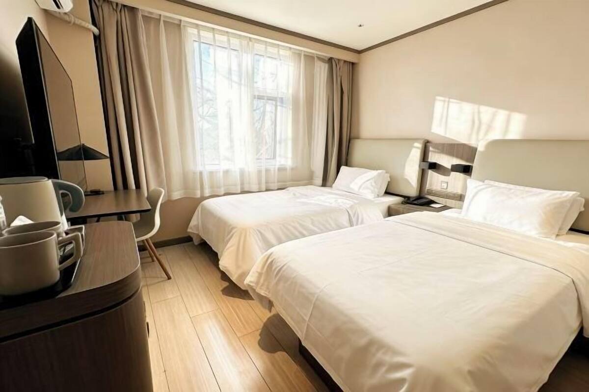 A hotel room with two beds, a desk with a chair, a TV, and a window with curtains.