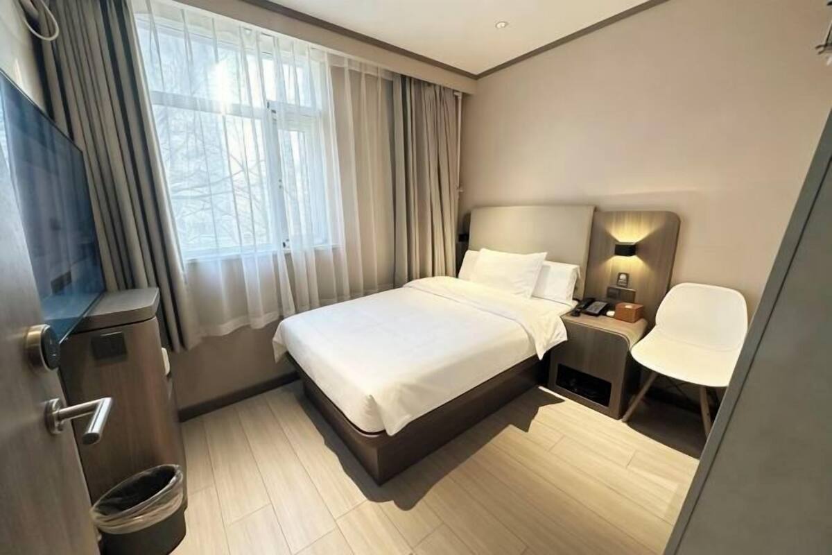 A modern hotel room with a bed, bedside table, lamp, chair, and a TV.