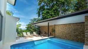 A modern outdoor swimming pool with lounge chairs and a stone wall. - Casa Dos Cascadas - Luxury & Jungle (Manuel Antonio)