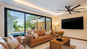 A modern living room with a brown leather sofa, a wooden coffee table, and a large TV mounted on the wall. - Casa Dos Cascadas - Luxury & Jungle (Manuel Antonio)