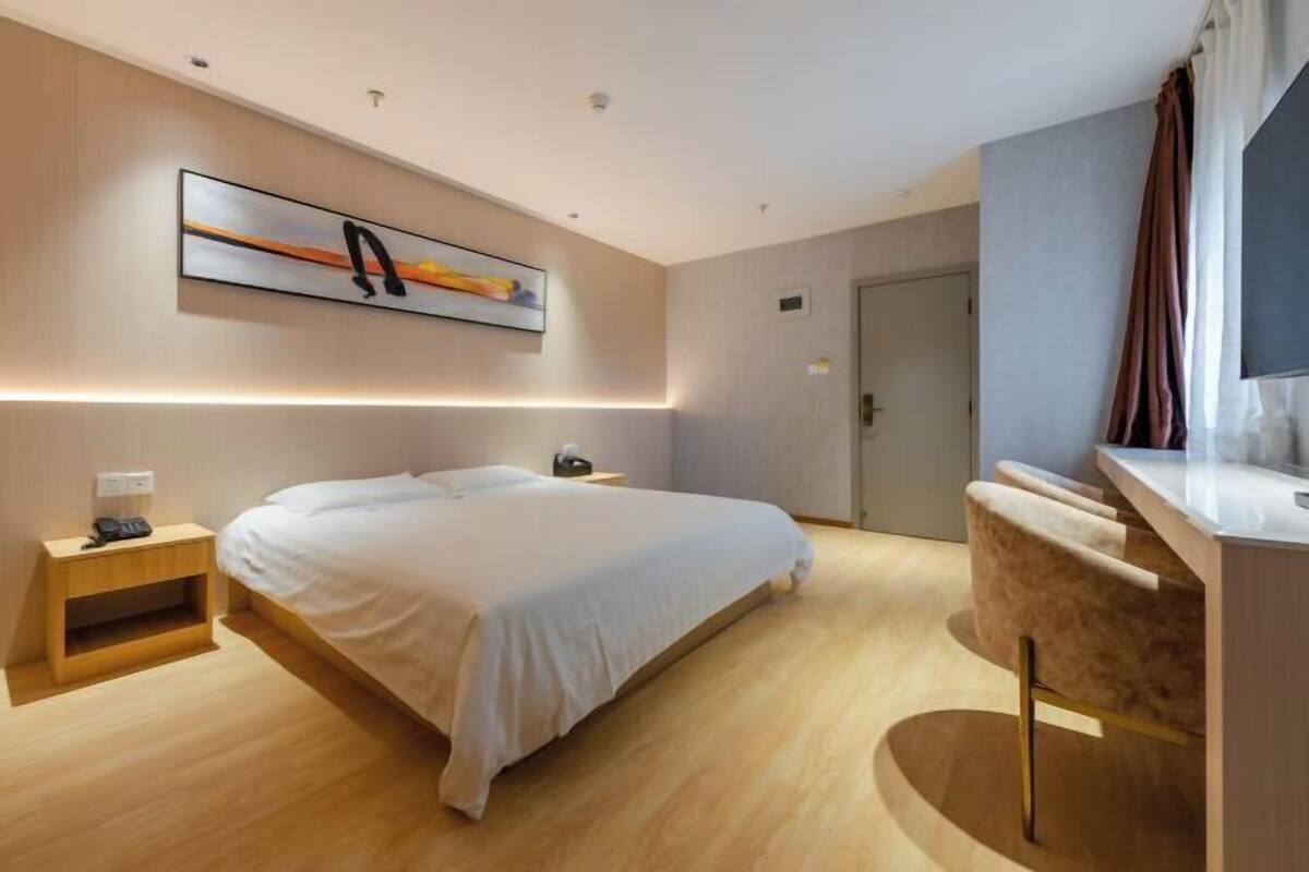 A modern hotel room with a large bed, bedside tables, a desk, and a painting on the wall.