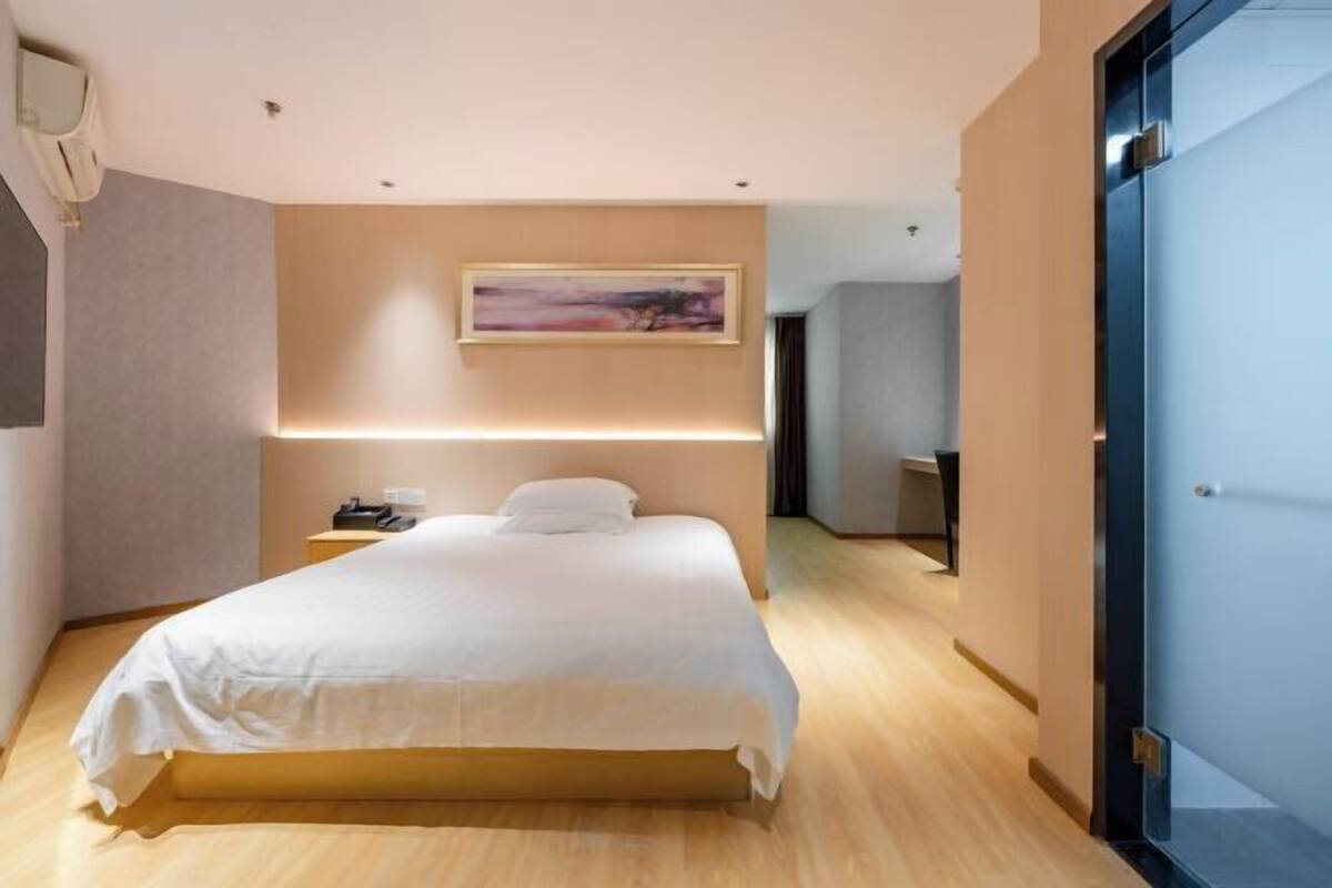 A modern hotel room with a large bed, a bedside table, a nightstand, and a painting on the wall.