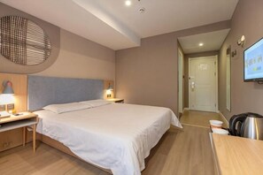 A hotel room with a large bed, bedside tables with lamps, a desk, a chair, a TV, and a door leading to another room.