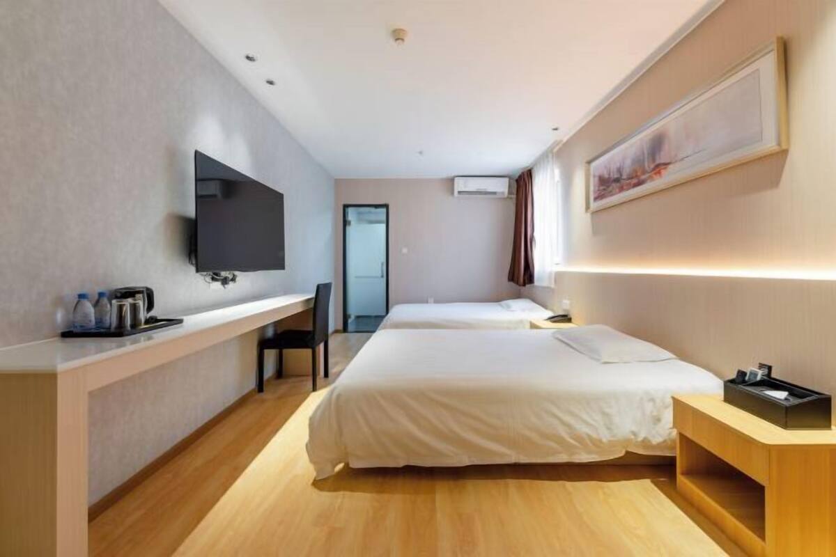 A hotel room with a bed, a desk with a flat-screen TV, a chair, and a bedside table.