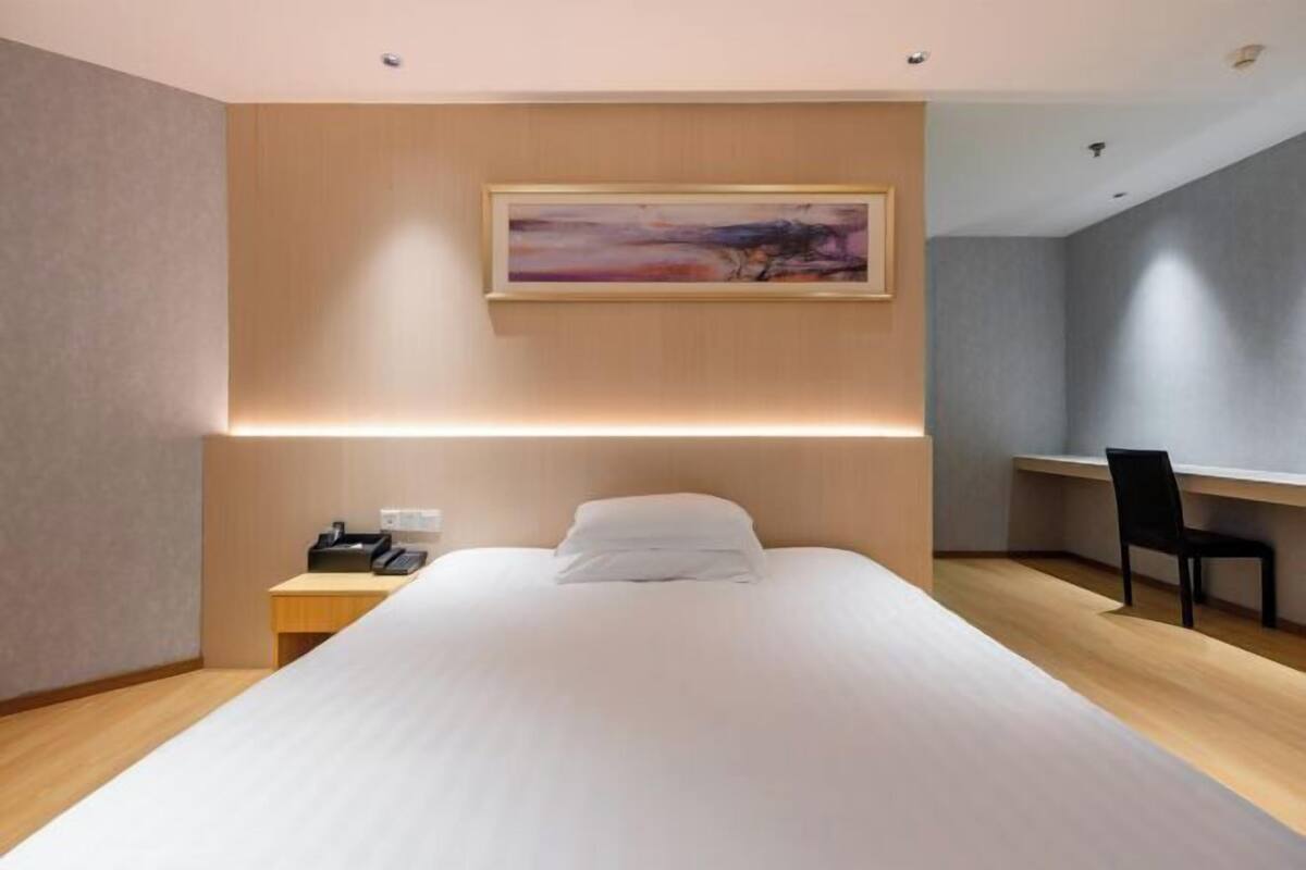 A modern hotel room with a bed, bedside table, chair, desk, and a painting on the wall.