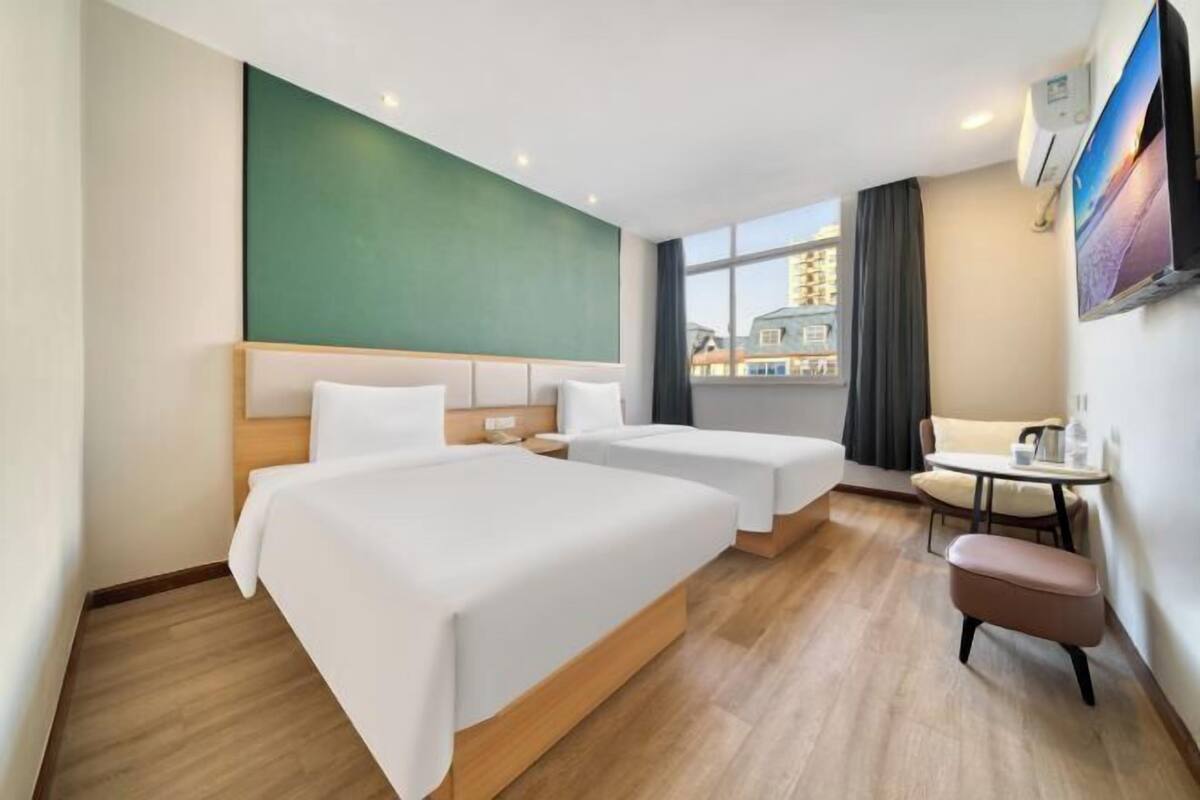A hotel room with two beds, a small table, a chair, and a window with a city view.