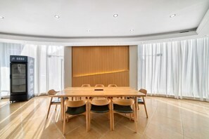 A conference room with a long table and chairs, a vending machine, and a large window with curtains.