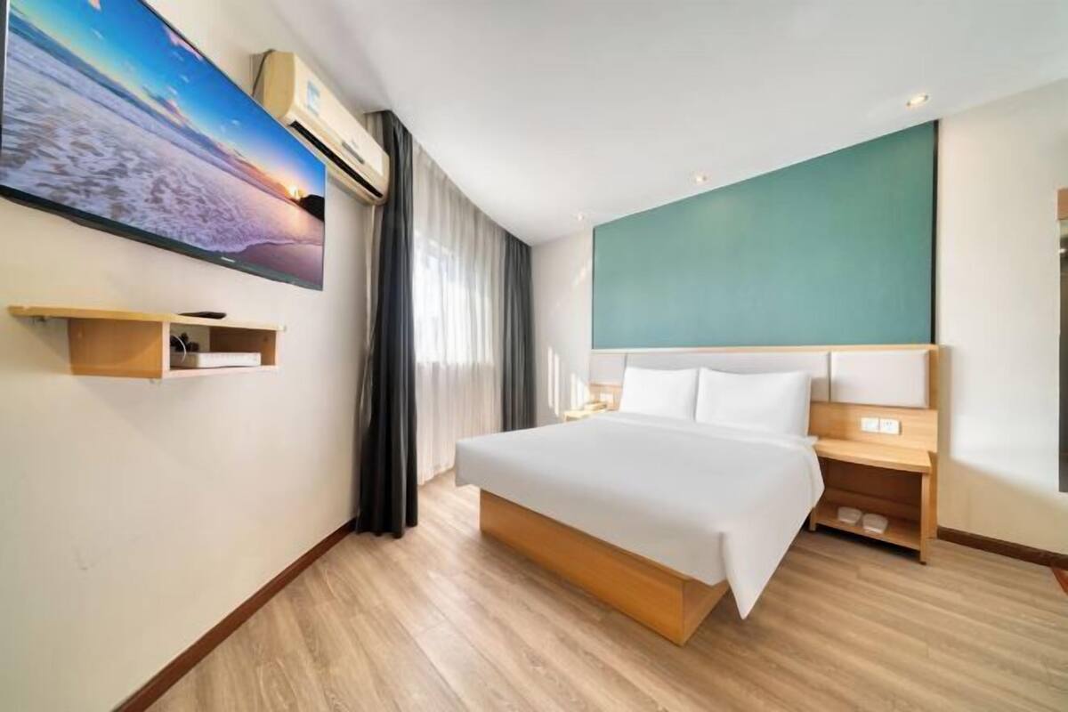 A hotel room with a bed, a TV, a desk, and a window with curtains.