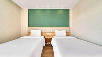 Une chambre d’hôtel avec deux lits simples, une table de chevet en bois avec un téléphone et un mur d’accent vert.