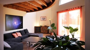 Una sala de estar moderna con un sofá seccional, una mesa de centro, un cuadro de una nebulosa, una planta en maceta y un ventanal con cortinas.