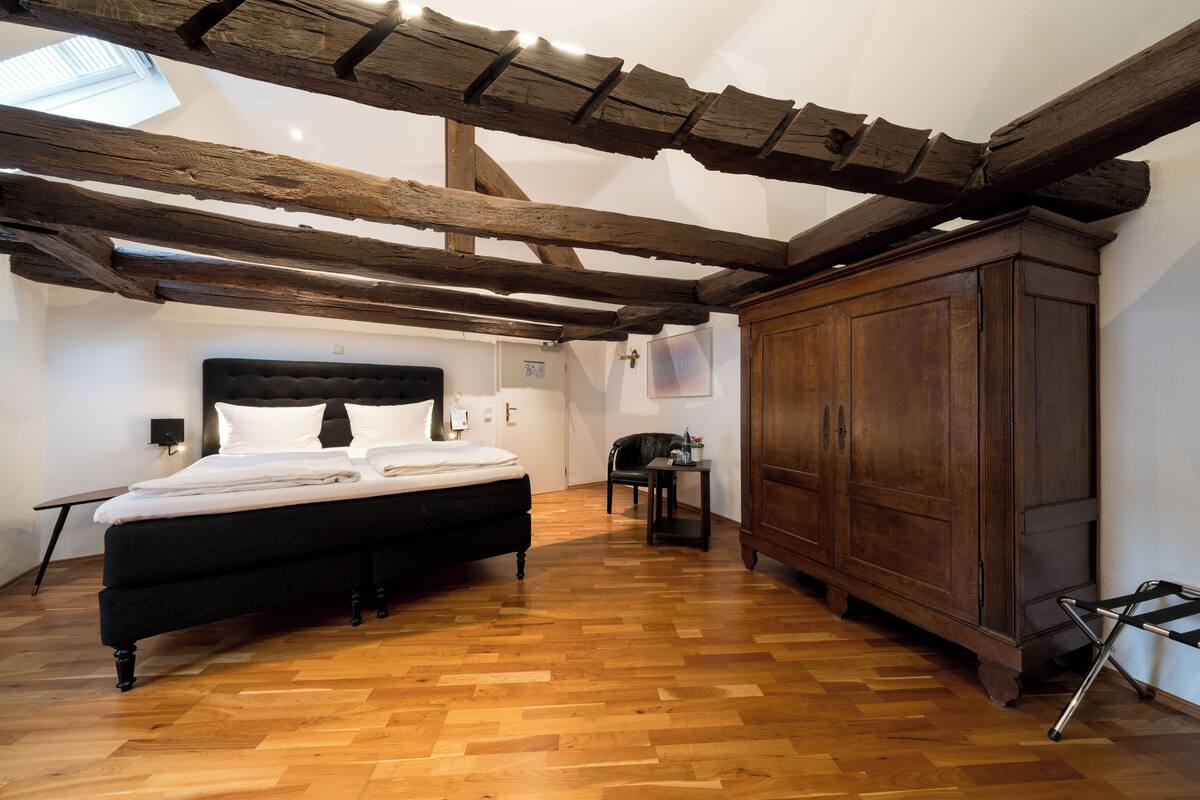 Une chambre avec un plafond en bois, un lit, une armoire et une petite table.