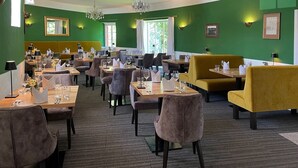 Ein Restaurant mit grünen Wänden, mehreren Tischen und Stühlen.