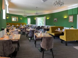 Un restaurante con paredes verdes, varias mesas y sillas.