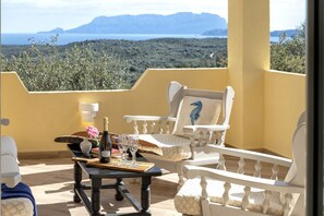 Ein Balkon mit Tisch für Zwei, ausgestattet mit einer Weinflasche, Gläsern und einem dekorativen Gegenstand. Der Balkon bietet Blick auf eine Berglandschaft.