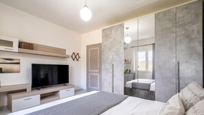 Un dormitorio moderno con cama, televisor, armario y un espejo grande.