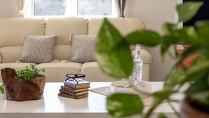 Una sala de estar con un sofá, una mesa de centro, una planta, libros y un florero de vidrio.