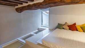 Ein Schlafzimmer mit Dachfenster, einem Bett mit farbenfrohen Kissen und einem Holzbalken darüber.