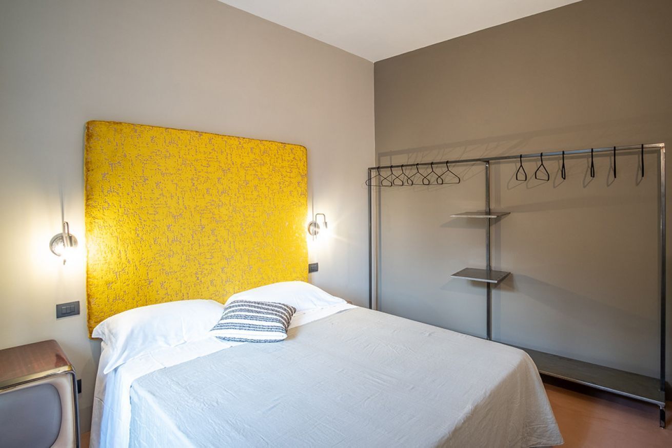 A hotel room with a bed, a wardrobe, and a wall-mounted light fixture.