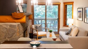 Un salon chaleureux avec un mur d’accent en pierre, une table basse en bois, un canapé et une table à manger agrémentée d’un saladier.