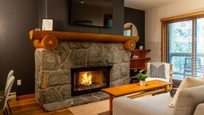 Un salon doté d’une cheminée en pierre, d’un téléviseur à écran plat fixé au-dessus et d’une fenêtre avec des stores.