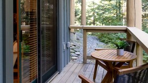 Une terrasse en bois avec une table et des chaises, un pot de fleurs et un chemin en pierre.
