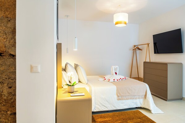 A hotel room with a bed, bedside table, lamp, TV, and a wooden hanger.
