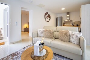 Un salon moderne avec un canapé beige, une table basse en bois sur laquelle repose une bouteille de champagne, et une carte du monde accrochée au mur.